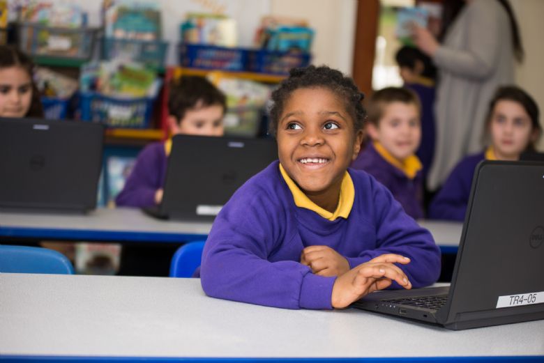 pupil looks up smiling from their laptop in the classroom